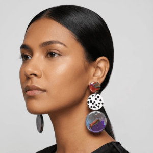 Model wearing marbled statement earrings with a red top disc, a white black polka dot middle disc, and a purple-blue marbled drop.