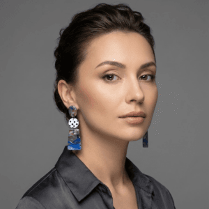 Model wearing handmade earrings with a marbled top disc, white black polka dot middle disc, and glossy purple-blue marbled bottom disc.
