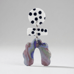 Close-up of polka dot earrings with a white black polka dot round stud, polka dot bar connector, and a marbled scalloped arch drop on a light grey background.