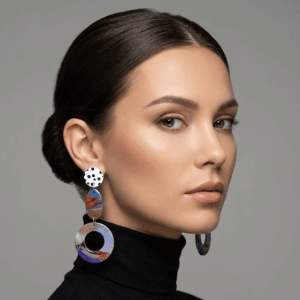 Model wearing bold earrings with a white black polka dot stud, marbled oval connector in orange-blue tones, and a large marbled hoop drop in purple and pastel swirls.