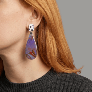 Model wearing fimo earrings with a white black polka dot stud and a purple-blue-red marbled teardrop drop.