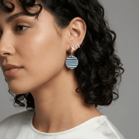 close-up of handcrafted jewelry featuring striped polymer clay hanging earrings with gold square studs, worn by a woman from blueberry bloom collection
