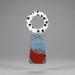 Close-up of flower earrings with a white scalloped ring top with black dots and a marbled blue-red trapeze drop on a light grey background.