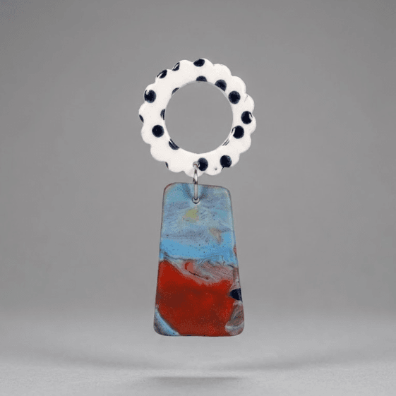 Close-up of flower earrings with a white scalloped ring top with black dots and a marbled blue-red trapeze drop on a light grey background.