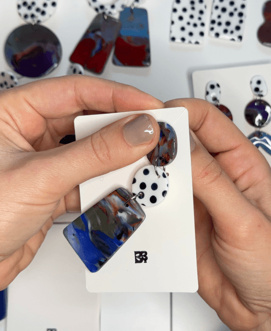 Artisan earrings brand owner in Vienna holding handmade polymer clay earrings in her studio.
