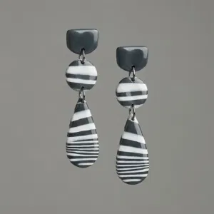 close-up of handmade glossy statement earrings with black and white striped polymer clay drops and stainless steel studs, part of blueberry bloom earring design collection