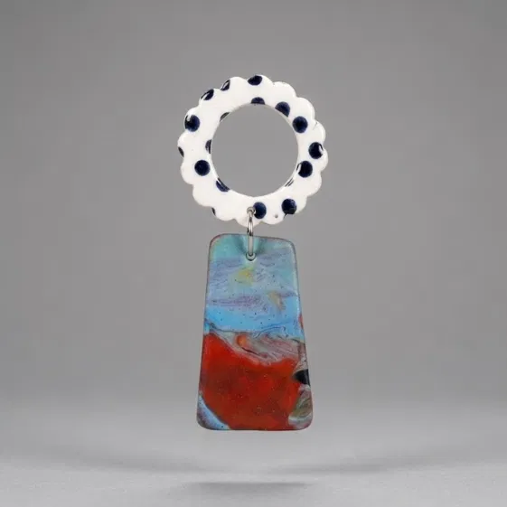 Close-up of flower earrings with a white scalloped ring top with black dots and a marbled blue-red trapeze drop on a light grey background.