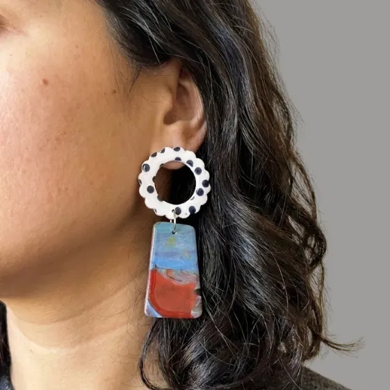 Model wearing flower earrings with a white scalloped ring top with black dots and a marbled blue-red trapeze drop.