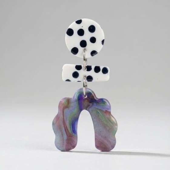 Nahaufnahme von Polka-Dot-Ohrringen mit rundem schwarz-weiß gepunktetem Stecker, gepunktetem Stab-Verbinder und marmoriertem, gewellten Bogen-Anhänger vor hellgrauem Hintergrund.