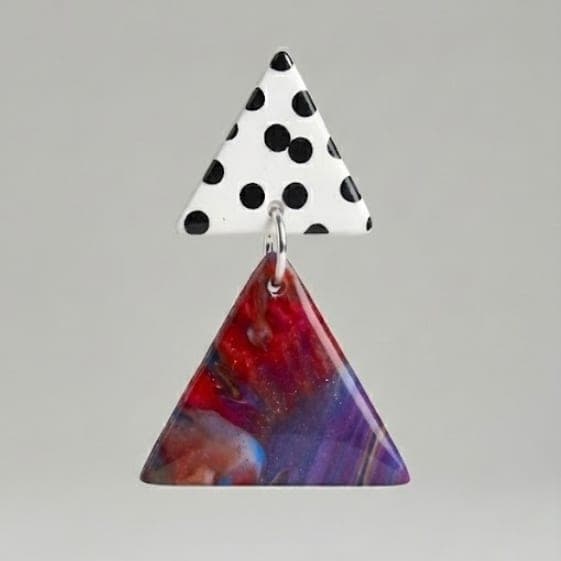 Close-up of dangle earrings with a white black polka dot triangle stud and a marbled purple-red triangle drop on a light grey background.