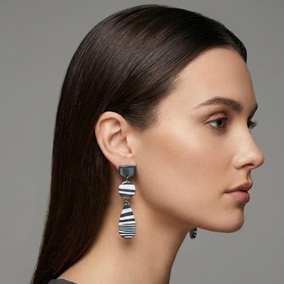 close-up of handmade statement earrings with zebra-striped polymer clay drops and stainless steel posts, worn by a woman for blueberry bloom