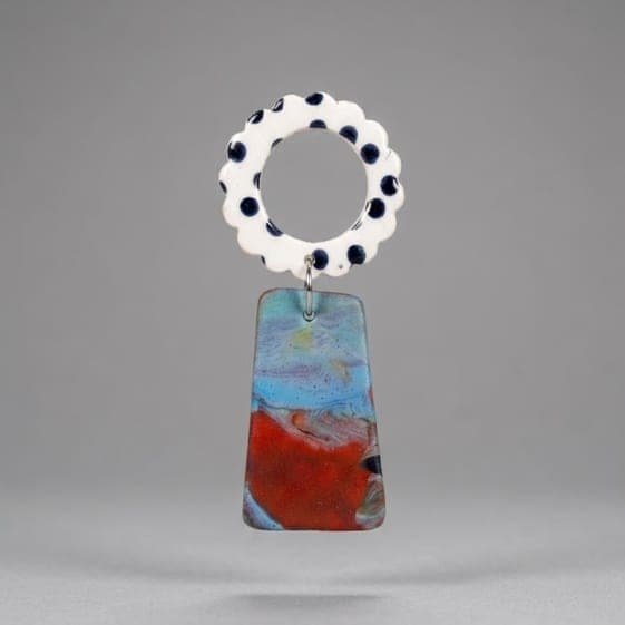 Close-up of flower earrings with a white scalloped ring top with black dots and a marbled blue-red trapeze drop on a light grey background.